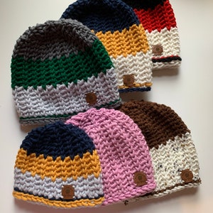 May include: Six colourful crocheted beanies with different colour combinations. Each beanie has a brown leather tag with a small tree logo.