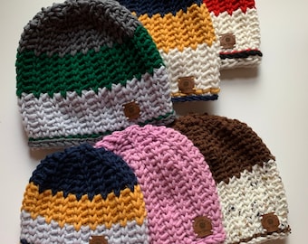 May include: Six colorful crocheted beanies with different color combinations. Each beanie has a brown leather tag with a small tree logo.
