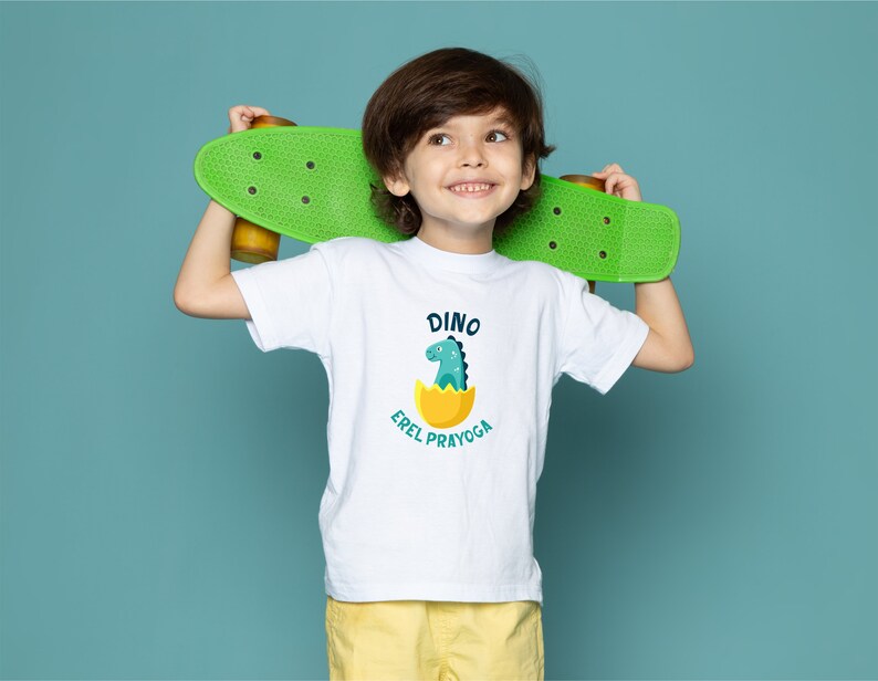 May include: A white t-shirt with a green dinosaur in an egg graphic and the text "Dino Errel Prayoga". A young person is wearing the shirt and holding a green skateboard behind their back.