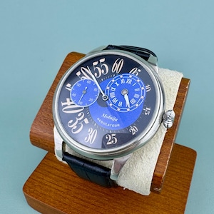 May include: A black and silver Molnija Regulator watch with a black leather band. The watch face features a blue subdial and a blue center dial with white numerals. The watch is displayed on a wooden stand.