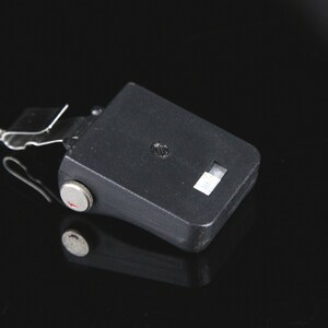 Pode incluir: Uma unidade de flash preta com uma manivela prateada e uma pequena janela branca. A unidade de flash est&aacute; conectada a um cabo preto.