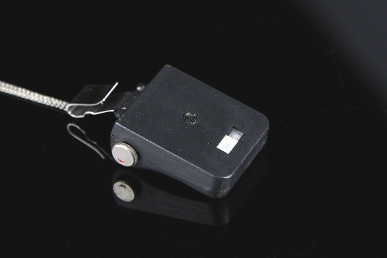 Pode incluir: Uma unidade de flash preta com uma manivela prateada e uma pequena janela branca. A unidade de flash est&aacute; conectada a um cabo preto.