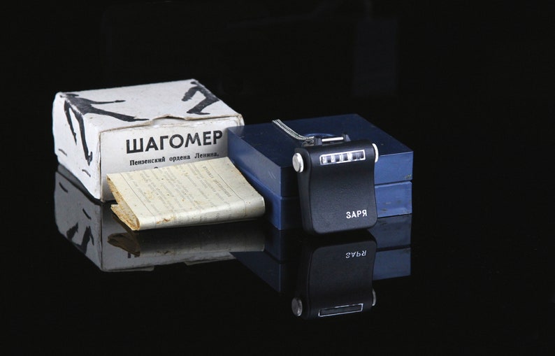 Pode incluir: Um ped&ocirc;metro preto com um visor digital e o texto "ЗАПР" no lado. O ped&ocirc;metro est&aacute; em uma caixa azul com o texto "ШАГОМЕР Пензенский ордена Ленина..." na parte superior de uma caixa branca.