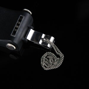 Pode incluir: Um dispositivo preto com um clipe e uma corrente prateados. O dispositivo tem um bot&atilde;o vermelho e a palavra "ЗАРЯ" impressa nele.