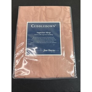 Puede incluir: Un juego de ropa de cama color rosa empolvado empaquetado en plástico transparente. La tela presenta un patrón de damasco tonal. Una etiqueta rectangular azul oscuro está centrada en el frente con el texto CUDDLEDOWN Superior Sleep starts with superior bedding.