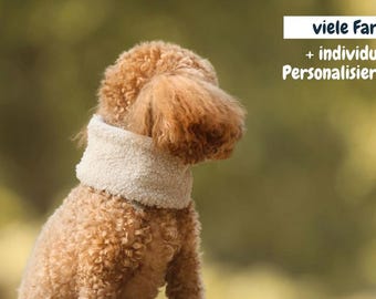May include: A brown poodle wearing a cream-colored, fluffy scarf. The dog is facing away from the camera, with a blurred green and yellow background. Text in the upper right corner reads "viele Farben + individuelle Personalisierung."