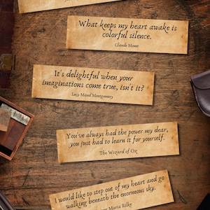 May include: A wooden surface displays several aged paper rectangles with quotes from famous authors. A pocket watch, a small wooden box, a pen, and a phone are also visible. The quotes are from John Wyndham, Claude Monet, Lucy Maud Montgomery, The Wizard of Oz, and Rainer Maria Rilke.