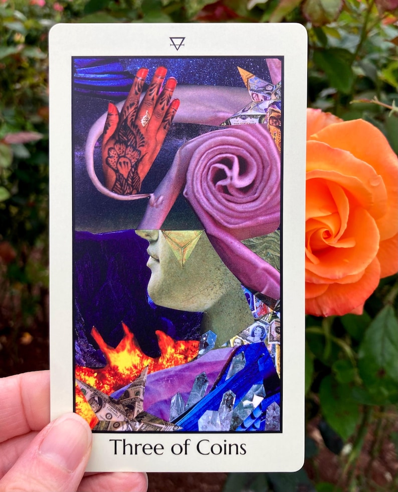 May include: A tarot card with a collage design featuring a hand with henna, a pink spiral, and a profile with a gold triangle. The card reads "Three of Coins" at the bottom. An orange rose is in the background.