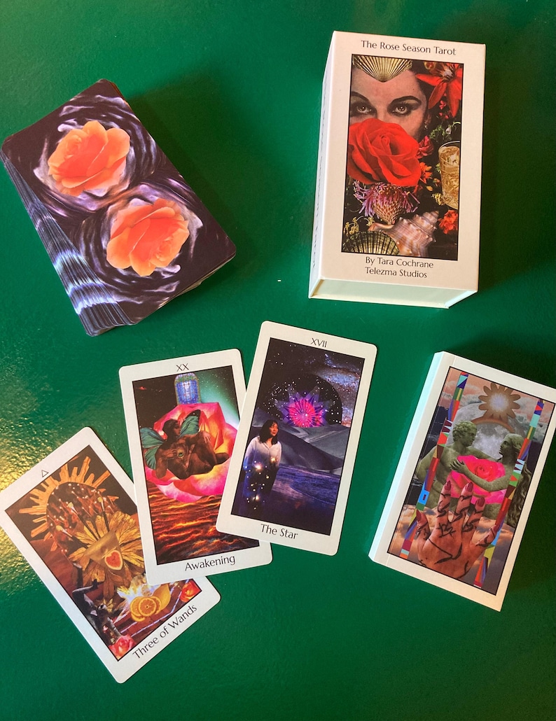 May include: A tarot card deck and several individual cards are displayed on a green surface. The deck box features an image of a woman with a red rose. Individual cards show various illustrations and the text "Awakening", "The Star", and "Three of Wands".