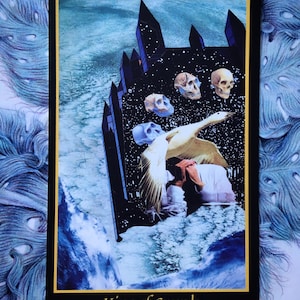 On the King of Swords card from the Telezma Tarot, the king is seen in his obsidian sky fortress high above the Earth. His hands are folded in reverie as the goose of imagination takes flight, with four skulls showing the path of human evolution.