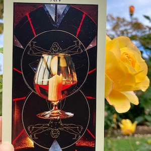 May include: A tarot card with the Roman numeral XIV at the top and the word "Art" at the bottom. The card features a wine glass with a candle inside, set against a dark background with geometric shapes and a human figure.