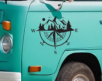 May include: A teal blue van with a black compass decal featuring a mountain range, trees, and deer. The compass points are labeled with the letters N, S, E, W, and the cardinal directions are labeled with the abbreviations NW, SE, SW, NE.