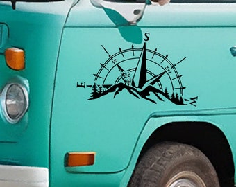 May include: A black and white compass sticker with a mountain range and a pine tree forest design. The compass points north, south, east, and west. The sticker is on a teal blue van.