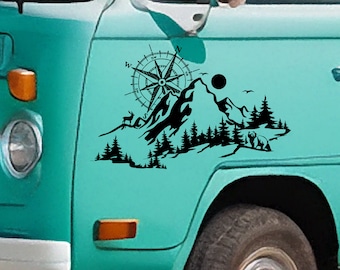 May include: Black and white silhouette decal of a mountain range with a compass, deer, bear, and trees. The decal is applied to the side of a teal blue van.