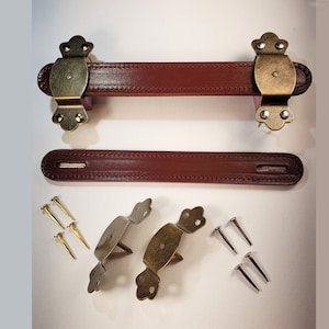 May include: Two sets of brown leather handles with brass hardware. Each handle has two decorative brass pieces with a floral design. The handles are accompanied by four brass screws.