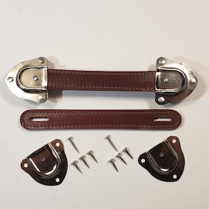 May include: A set of brown leather handles with metal clasps and screws. The handles are designed for attaching to a suitcase or other luggage.