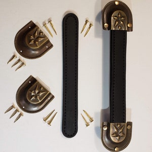 May include: Two black leather handles with brass star-shaped accents and decorative trim. The handles are attached to the brass accents with small brass tacks. The handles are shown with additional brass tacks.