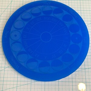 May include: A blue plastic moon phase tracker with Roman numerals and the words "Full", "Half", "Waxing", and "Waning" around the edge.