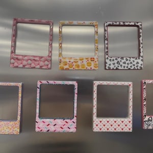 以下が含まれることがあります： ハート、絵文字、抽象的なデザインなど、さまざまなパターンが施された7つの装飾的なフォトフレーム。 フレームは長方形で中央が透明で、パターンはピンク、黄色、黒、白です。