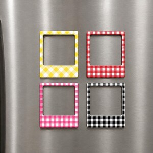 May include: Four square magnetic photo frames with a gingham pattern. The frames are arranged in a grid, featuring yellow, red, pink, and black and white checkered designs. Each frame has a wide bottom border and a thin top and side border.