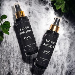 May include: Two black glass bottles with gold spray tops and black labels. The labels have white text that reads "KREED FOR HIM CAR FRESHENER ALWAYSROSY.CO.UK 100ml" and "SNOW ANGELS CAR FRESHENER ALWAYSROSY.CO.UK 100ml".