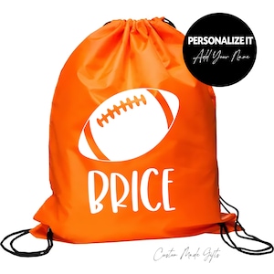 May include: Orange drawstring bag with a white football and the name "PRICE" printed on it. The bag has black drawstrings.  "PERSONALIZE IT Add Your Name" is printed on a black circle.