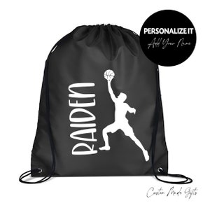 May include: Black drawstring bag with a white basketball player silhouette and the name "RAIDEN" printed on it. The bag has a white drawstring and is personalized with the option to add a name.