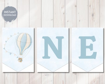 May include: A printable banner for a first birthday party. The banner has three sections, one with a blue and white hot air balloon, one with the letter N, and one with the letter E. The background is a light blue watercolor wash.