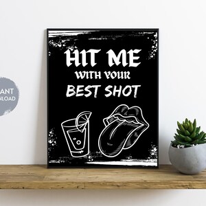 May include: Black and white printable wall art with the text "Hit me with your best shot" and illustrations of a shot glass with a lime wedge and a tongue sticking out.