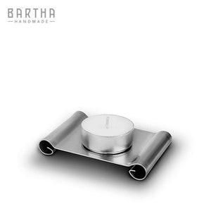 Könnte beinhalten: Ein silberner Kerzenhalter aus Metall mit gerollten Design. Eine weiße Teelichtkerze sitzt in der Mitte des Halters.
