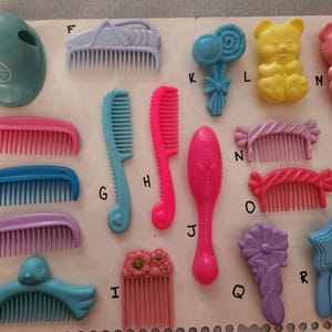 May include: Collection of colorful plastic hair accessories, including combs and a hair helmet. The items are in various shapes and colors, such as pink, blue, yellow, and purple. Some combs have decorative elements like flowers and bows.
