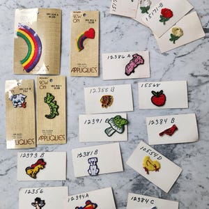 May include: A collection of vintage sew-on appliques, including a rainbow, heart with rainbow, flowers, animals, and other designs. The appliques are on small cards with product numbers and prices.