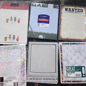 May include: Six packages of decorative stationery paper. Top row: cactus print paper, golf-themed letterhead, and a parchment-style paper with the word WANTED. Bottom row: map-patterned paper, a computer monitor design, and a golf ball border design.