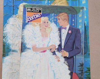 May include: A vintage Barbie 100-piece puzzle featuring a romantic illustration of Barbie in a white gown with a male companion in a tuxedo. The puzzle box is visible, showing the Barbie logo and puzzle details.