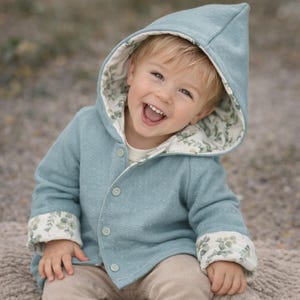 Puede incluir: Chaqueta con capucha azul claro con textura de gofre. La capucha y los puños están forrados con un estampado floral. La chaqueta está abotonada y parece estar hecha de una tela suave.