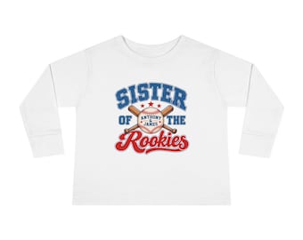 May include: A white long-sleeve shirt featuring a graphic of two crossed baseball bats behind a baseball. The text reads SISTER OF THE ROOKIES with ANTHONY & JAMES printed on the baseball in blue and red lettering with three stars.