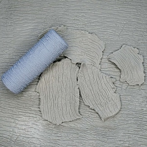 May include: A close-up of a paint roller with a textured surface, and a gray textured surface with a pattern of lines. The paint roller is partially on the textured surface.