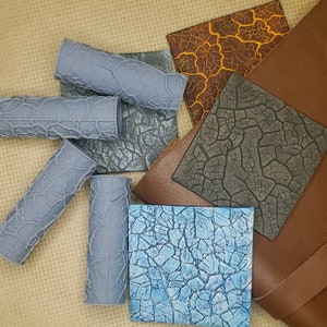 May include: A set of six gray textured paint rollers, some with a blue hue, arranged on a brown and gray patterned surface. The surface is made of a textured material that resembles cracked paint.