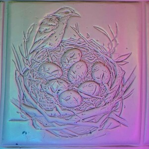 K&ouml;nnte beinhalten: Eine wei&szlig;e Keramik-Reliefskulptur eines Vogels, der auf einem Nest mit Eiern sitzt. Der Vogel sitzt auf einem Ast und hat die Fl&uuml;gel ausgebreitet. Die Eier sind in einem Kreis um den Vogel angeordnet.