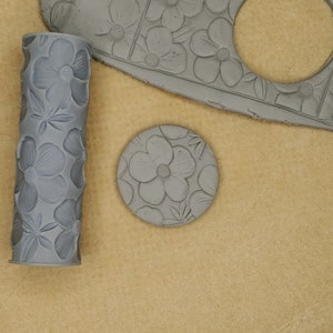 May include: A gray clay rolling pin with a floral design, a gray clay disc with a floral design, and a gray clay sheet with a floral design.