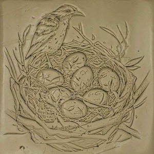 K&ouml;nnte beinhalten: Eine detaillierte Tonreliefskulptur eines Vogels, der auf einem Nest mit Eiern sitzt. Der Vogel sitzt am Rand des Nestes, die Fl&uuml;gel ausgebreitet. Die Eier sind in einem Kreis in der Mitte des Nestes angeordnet.