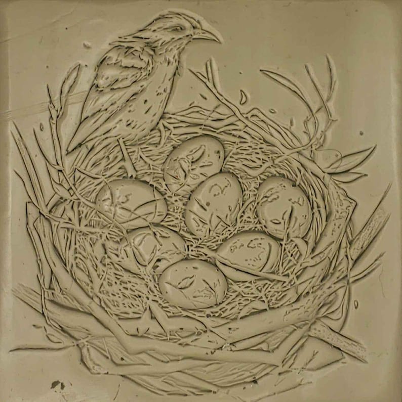 K&ouml;nnte beinhalten: Eine detaillierte Tonreliefskulptur eines Vogels, der auf einem Nest mit Eiern sitzt. Der Vogel sitzt am Rand des Nestes, die Fl&uuml;gel ausgebreitet. Die Eier sind in einem Kreis in der Mitte des Nestes angeordnet.