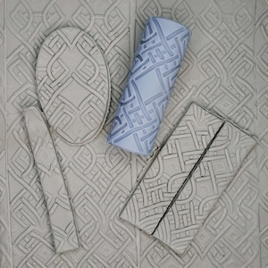 May include: A set of five gray textured rubber stamps with geometric patterns. The stamps are arranged on a gray background.