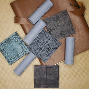May include: Five gray and black tile-like pieces with geometric patterns. The tiles are on a brown leather surface.