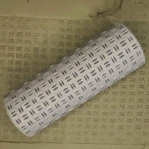 May include: A gray rolling pin with a diamond pattern. The rolling pin is made of a textured material and is designed for creating embossed patterns in clay or dough.