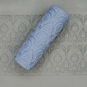 May include: A blue textured paint roller with a damask pattern. The roller is lying on a surface with a similar pattern.