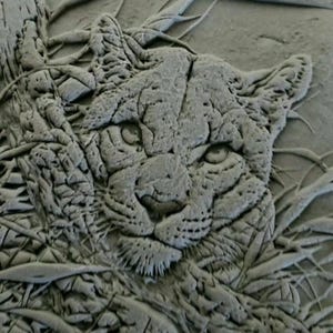 May include: A detailed, gray relief sculpture of a cougar's face, surrounded by stylized foliage. The cougar's features are intricately carved, showcasing its eyes, nose, and whiskers. The artwork has a textured appearance.