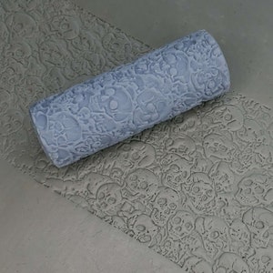 May include: A gray textured paint roller with a skull pattern. The roller is being used to create a skull pattern on a gray surface.