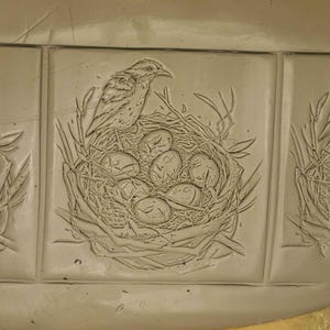 K&ouml;nnte beinhalten: Eine Keramikfliese mit einem gepr&auml;gten Design eines Vogels, der auf einem Nest mit Eiern sitzt.