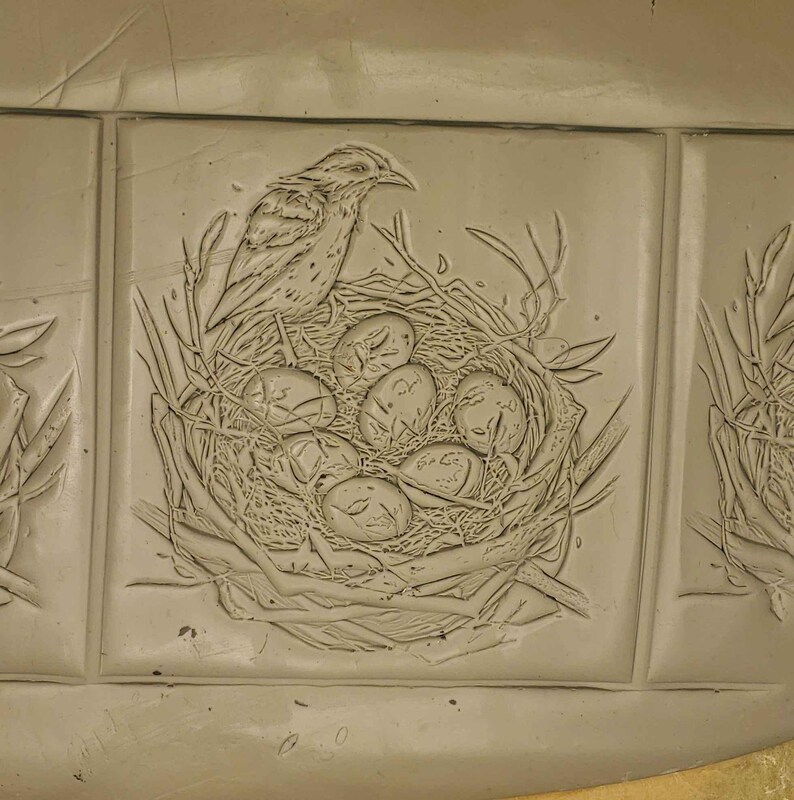 K&ouml;nnte beinhalten: Eine Keramikfliese mit einem gepr&auml;gten Design eines Vogels, der auf einem Nest mit Eiern sitzt.